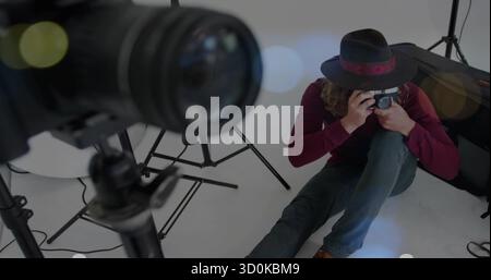 Kneeling photographer aiming mirrorless camera on studio floor, lights, tripod lens, copy space Stock Photo