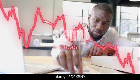 Reviewing documents on laptop, African American man sitting in modern office with red chart overlay Stock Photo