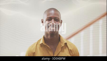 Smiling man wearing mustard-colored shirt leaning in modern office corridor, with wooden handrail Stock Photo