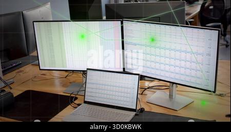Displaying dual-monitor setup showing spreadsheet map on office desk with laptop and cables Stock Photo