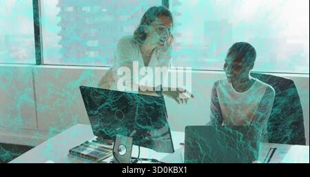 Collaborating two women wearing office attire examining data on monitor at office with notebooks Stock Photo