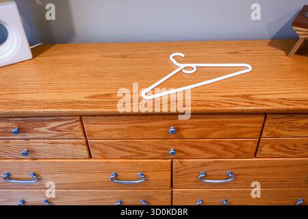 A white plastic clothes hanger lying on the top of the wooden dresser or chest of drawers. Stock Photo