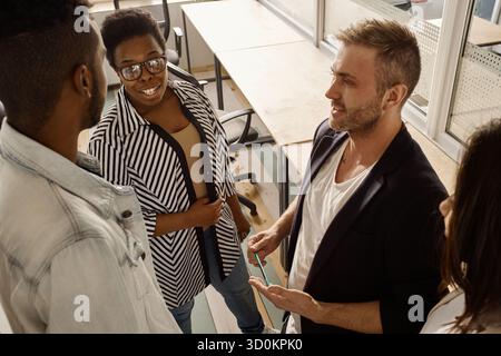 Multiethnic group of young colleagues standing in modern office, sharing their ideas on new project and smiling, high angle view Stock Photo