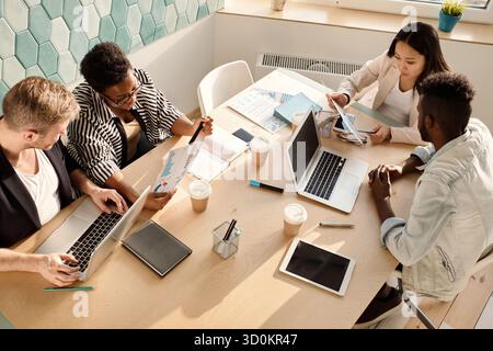 Multiethnic group of young managers sitting around table in conference room and discussing new company strategies, high angle view Stock Photo