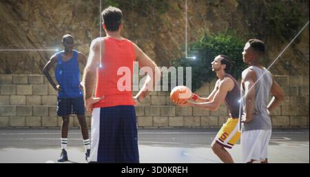 Four men in sportswear playing basketball on asphalt court with boundary lines and retaining wall Stock Photo