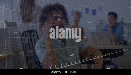 Talking mature Asian man in wheelchair using smartphone at office with laptops and chart overlay Stock Photo