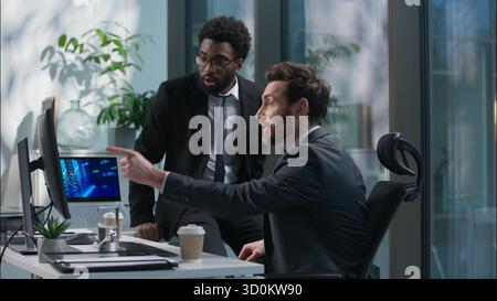 African American Caucasian men chatting talking break relax team businessmen business males looking computer monitor winning good news successful deal Stock Photo