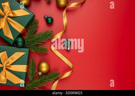 Two green gift boxes with golden bows on red background. Gift boxes,  fir tree branches, Christmas balls and golden ribbon on red. Stock Photo