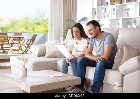 Happy couple reading paper letter sitting on a couch at home Stock Photo