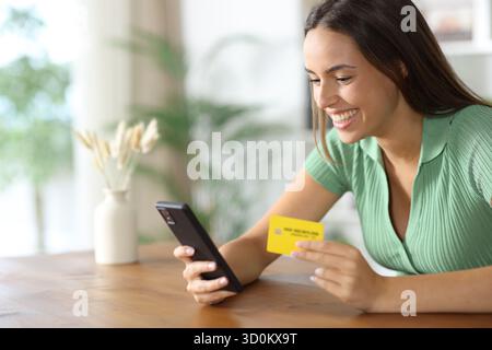 Happy woman using smart phone and credit card to buy online at home Stock Photo