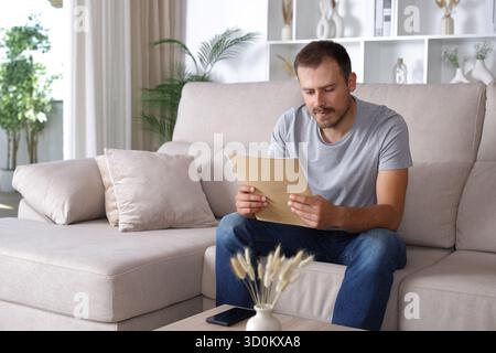 Serious man reading paper document sitting on a couch at home Stock Photo