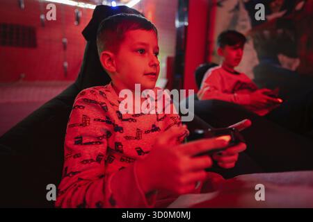Two boys gamers play gamepad video game console in red gaming room Stock Photo