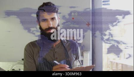 Writing bearded kitchen manager jotting notes on clipboard at restaurant kitchen, with world map Stock Photo