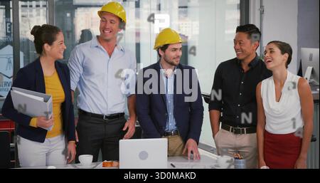 Reviewing blueprints by team wearing helmets in office meeting room, with laptop and tablet folder Stock Photo