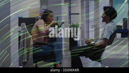 Two mid adult coworkers eating lunch in open-plan office area, with chopsticks and sandwich Stock Photo