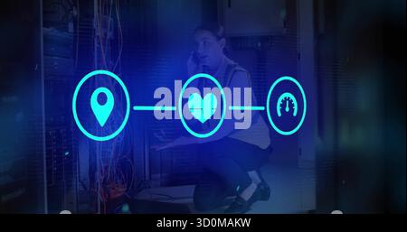 Kneeling technician wearing vest using phone, reaching for laptop in data center, icons, copy space Stock Photo