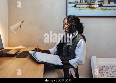 Young female architect working on a project, showcasing creativity and focus, seated at her desk. Stock Photo