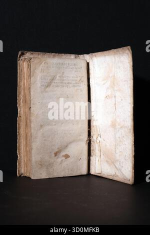 Open pages of a very old, deteriorated book (early print), showing aged, yellowed paper with ragged edges. displays visible text in old Italian/Latin. Stock Photo