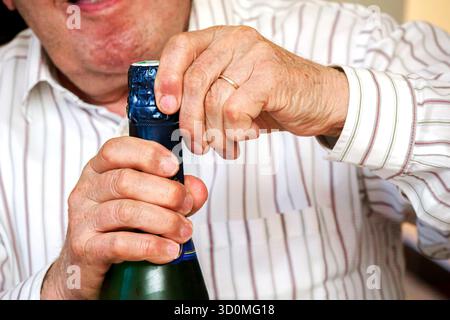 Close-up of a man opening a bottle of sparkling wine by hand, capturing a celebratory moment indoors. Stock Photo