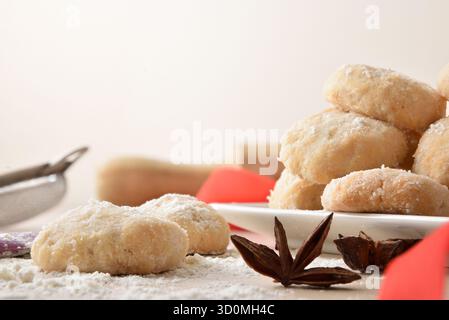 Detail of freshly baked anise cookies on a wooden table with kitchen utensils, flour, star anise and decorative red ribbon, isolated on white backgrou Stock Photo