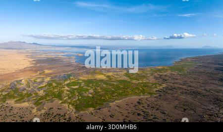 Aerial view of the sun-drenched volcanic landscape meeting the serene waters of Lake Natron, a symphony of earthy tones against the cool blue, Lake Natron, Maasai, Tanzania. Stock Photo