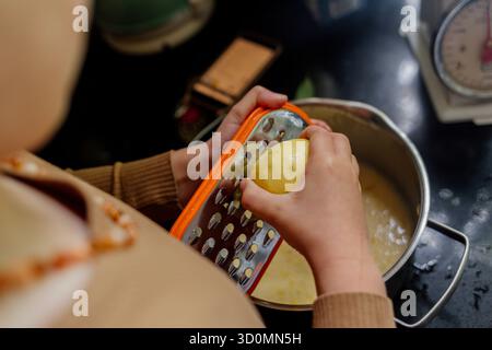Child grating lemon zest over bowl in kitchen Stock Photo
