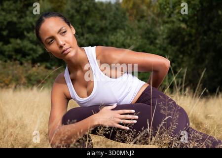 A young mixed-heritage woman practicing a yoga warrior twist pose in a golden autumn meadow, near London, United Kingdom. Photograph Stock Photo