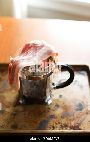 Raw slices of bacon over French press coffee maker Stock Photo
