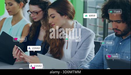 Typing team wearing business casual using laptops and tablets in office, showing social metrics Stock Photo