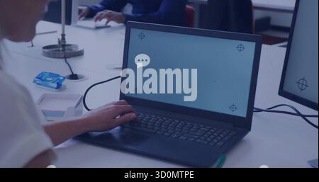 Mature office worker typing on black laptop in open-plan office, with task lamp and sticky notes Stock Photo