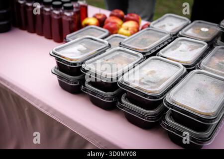 Plastic food containers with prepared meals stacked on table along with bottles and apples. Stock Photo