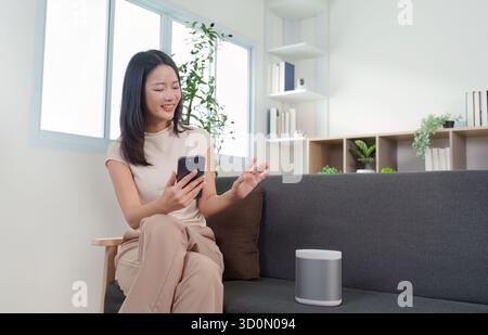 Smart Home: Woman interacting with smart speaker using smartphone Stock Photo