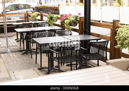 Outdoor restaurant terrace with empty tables. Wooden furniture in city cafe patio. No people present. Urban dining space ready for guests. Stock Photo