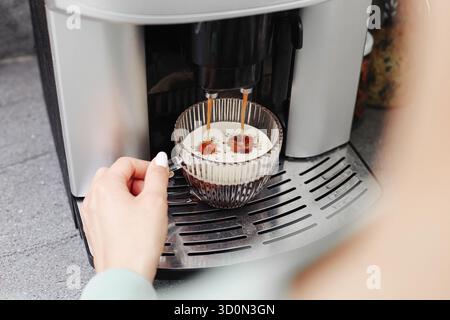 Coffee machine pouring espresso into glass cup. Home coffee preparation process. Fresh brewed coffee drink. Modern kitchen appliance in use. Stock Photo