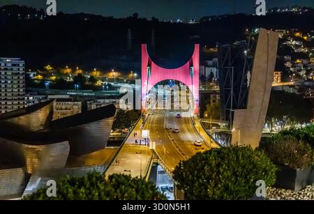 View of the illuminated red Puente de La Salve bridge over the Nervión River with cars under the dark sky, Bilbao, Spain. Stock Photo