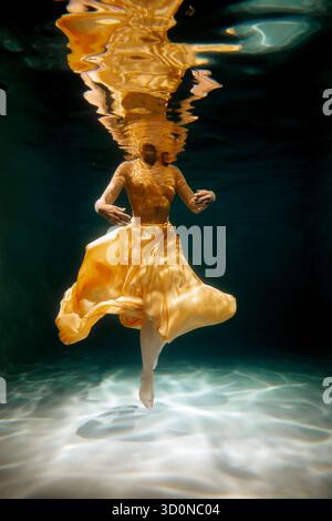 An Elegant Underwater Dance Captured in a Flowing Yellow Dress Beneath the Waves Stock Photo