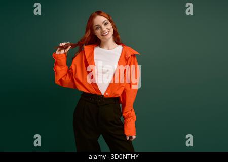A red-haired woman models autumn fashion in an orange shirt against green. Stock Photo