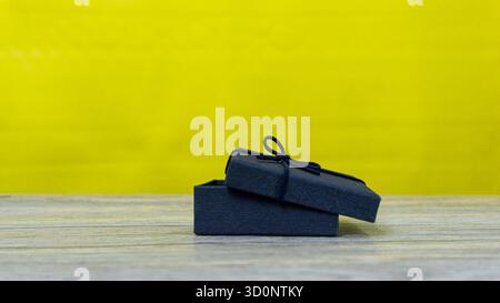 Open black gift box displayed on wooden table with vibrant yellow background, great for festive, celebration, or product display imagery. Stock Photo