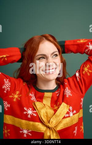 A red-haired woman showcases her cheerful personality in a Christmas sweater on a green backdrop. Stock Photo