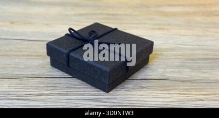 Closed black gift box resting on wooden table, ideal for packaging, gift-giving, retail, or holiday-themed visuals. Stock Photo