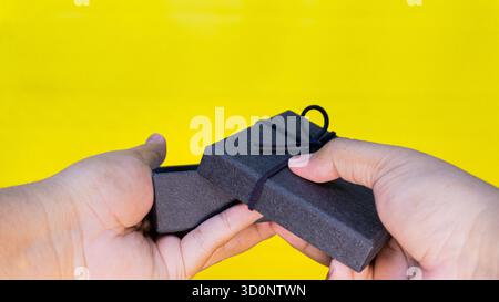 Open black gift box presented with both hands against a yellow background, great for celebration, surprise, or luxury gift imagery. Stock Photo