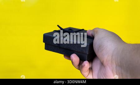 Closed black gift box in right hand against a yellow backdrop, ideal for product display, gifting, or festive celebration concepts. Stock Photo