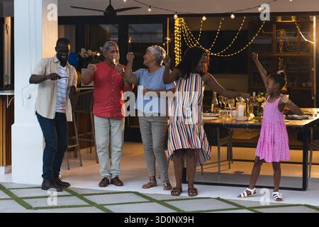 Family celebrating together outdoors, raising glasses and dancing joyfully at night. Celebration, party, family reunion, evening, togetherness, happiness || Model released Stock Photo