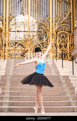 Ballet dancer standing in graceful pose in front of ornate golden gates at Petit Palais in Paris. Editorial use only due to recognizable architecture. Captured on June 15 2025. || Model released Stock Photo