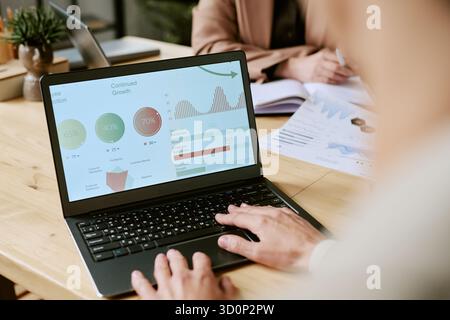 Young Adult Man Analyzing Business Data on Laptop in Office Setting Stock Photo