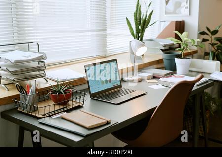 Modern Home Office Desk Featuring Laptop Displaying Business Analytics Charts Stock Photo