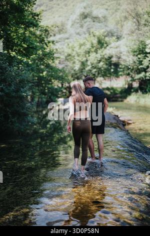 Couple walking together along a clear river surrounded by lush forest Stock Photo