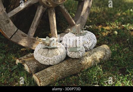 Handmade lace fabric pumpkins rest on cut logs near old wooden wagon wheel, rustic outdoor garden scene with cozy autumn mood Stock Photo