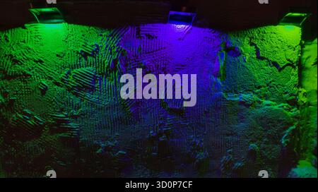 Rough plaster wall with heavy texture lit by green and blue neon, vivid moody glow creating dramatic abstract backdrop Stock Photo