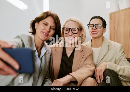 Three Middle Aged Women Smiling While Taking Selfie Indoors Stock Photo